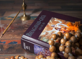 Bhagavad Gita and rosary lying on a wooden table and incense is being smoked.